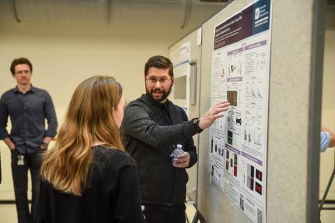 An NIH scientist points at a poster while an onlooker listens