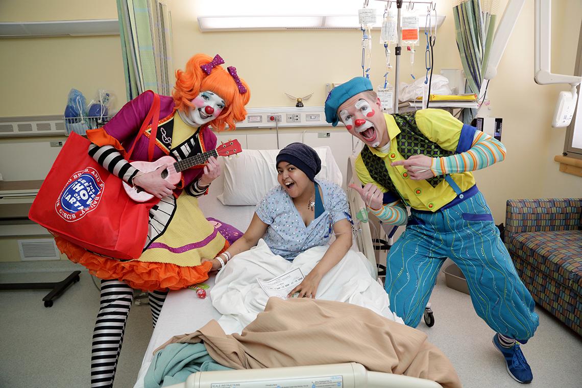 Clowns visit patient in her bed.