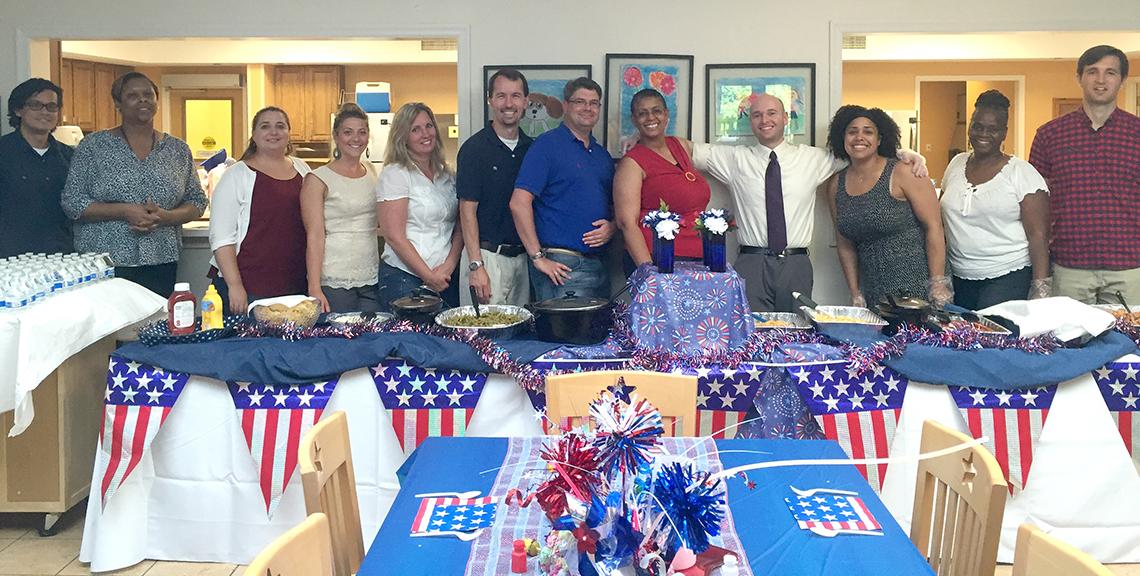 Large group of people face the camera behind a table adorned with patriotic quilt