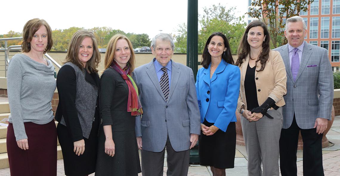 Group of seven people side-by-side smile for camera.