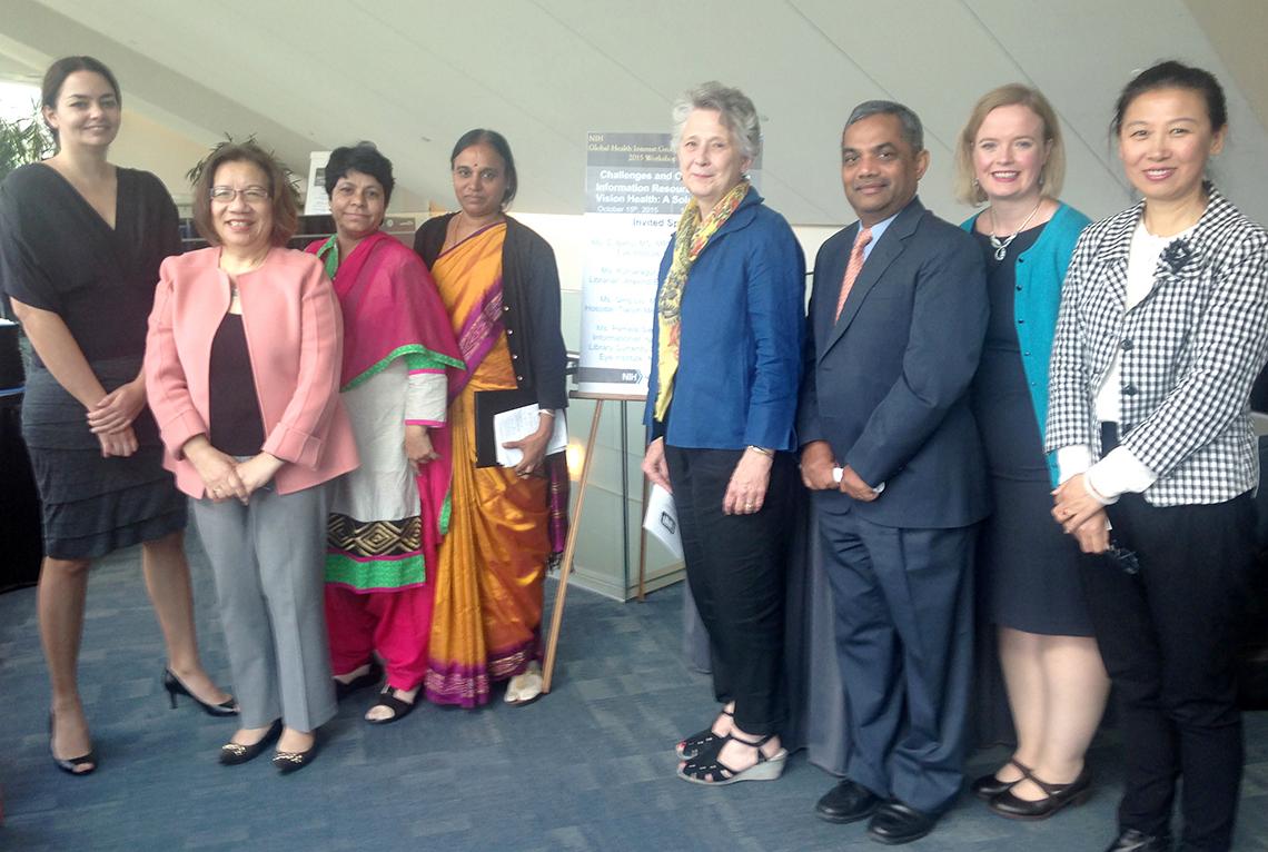 Group of eight people stand side-by-side, smiling for camera.