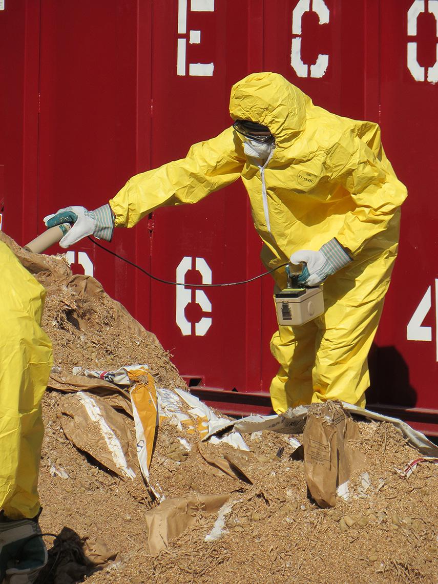 Person in hazmat suit, mask and gloves working on pile of dirt, landfill