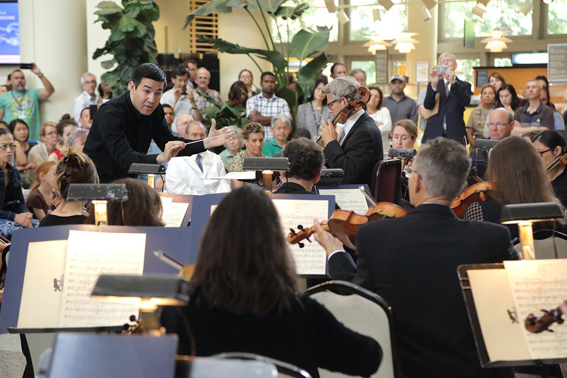 Conductor leads orchestra as NIH director looks on.