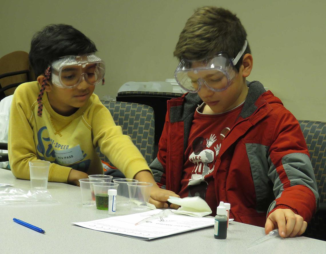 Two kids wear goggles and conduct an experiment