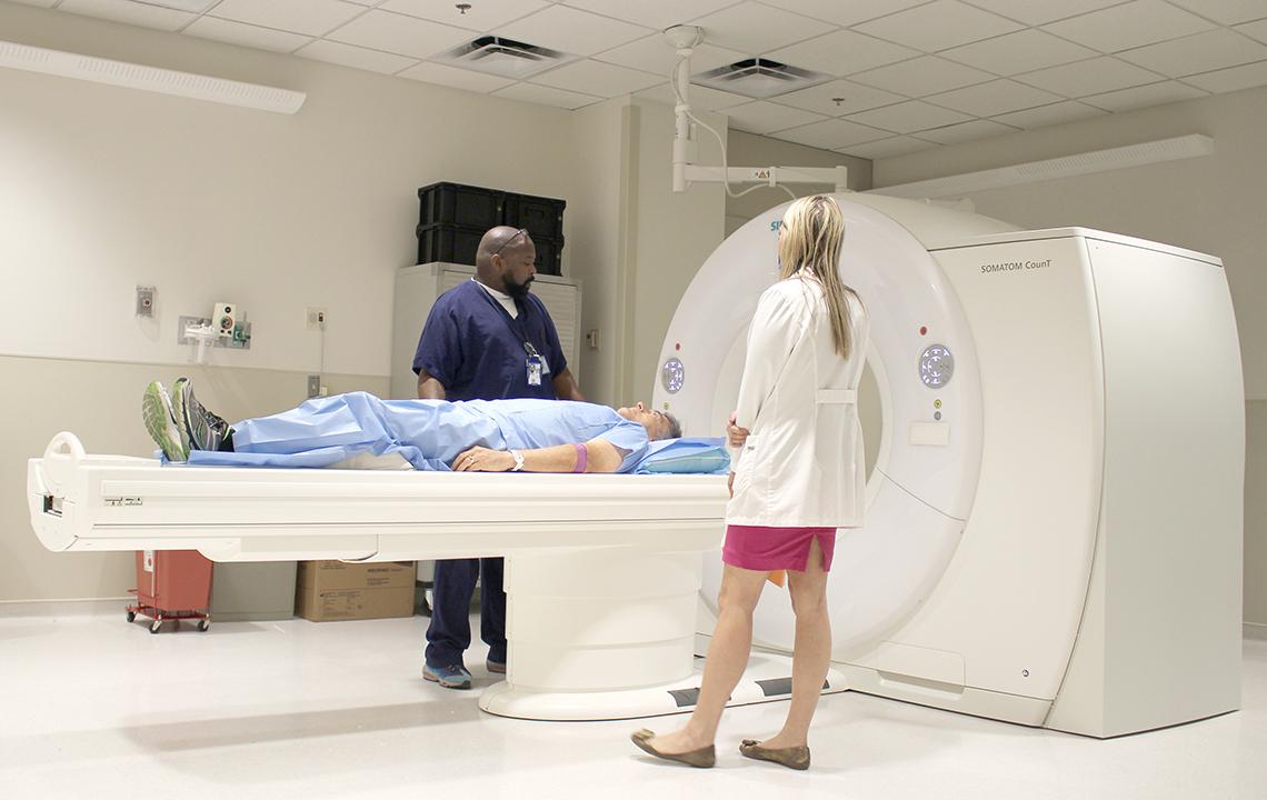 Individual lies on bed of new imaging machine as a tech stands on either side.