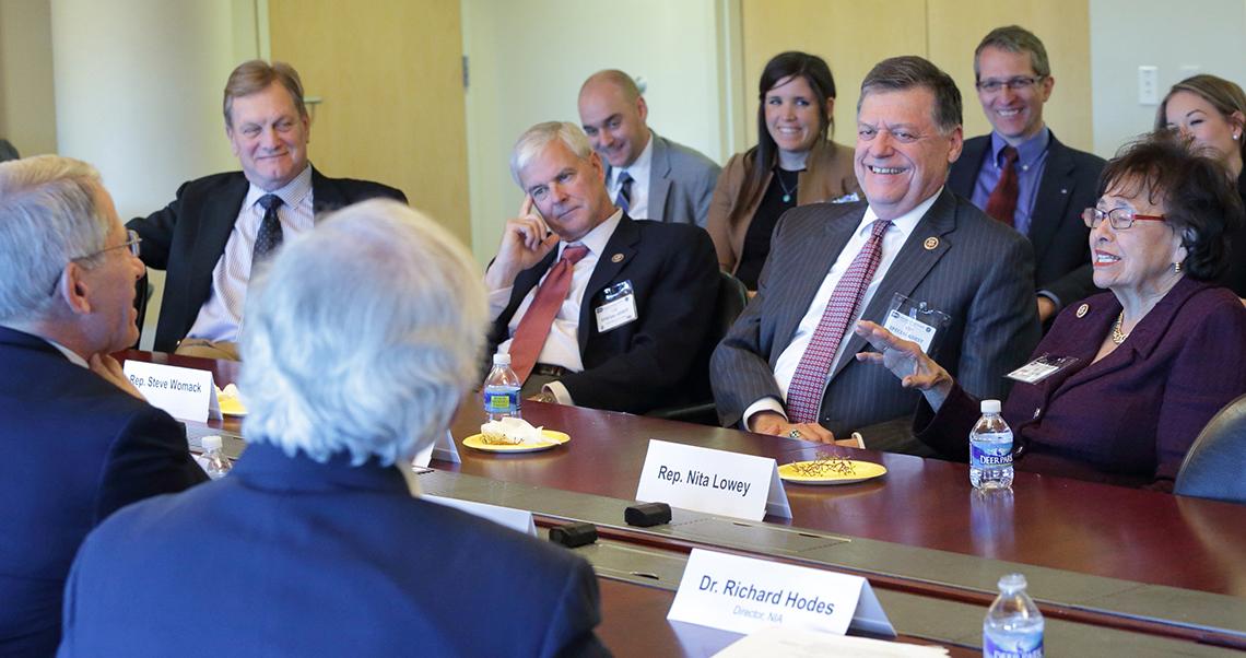 Visiting members of Congress sit, talking around board room table.
