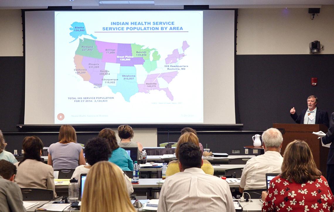 Dan Aune speaks to audience pointing to colorful slide of U.S. map from the Indian Health Service