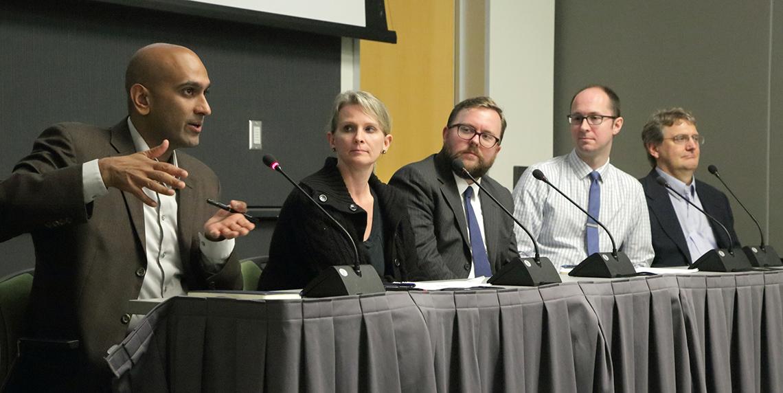 Seated at table, Patel speaks as panelists look on