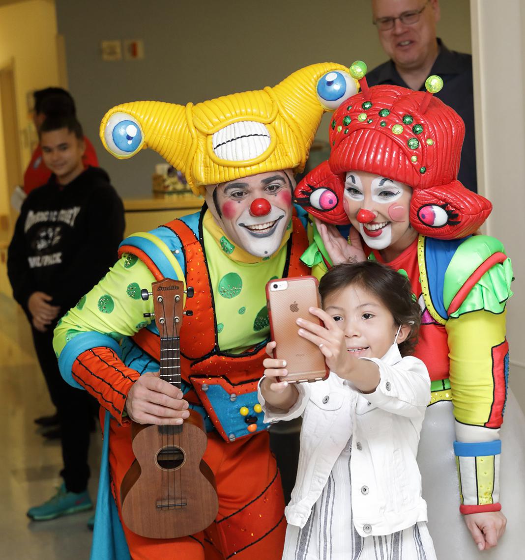 Young girl takes a selfie with circus clowns.
