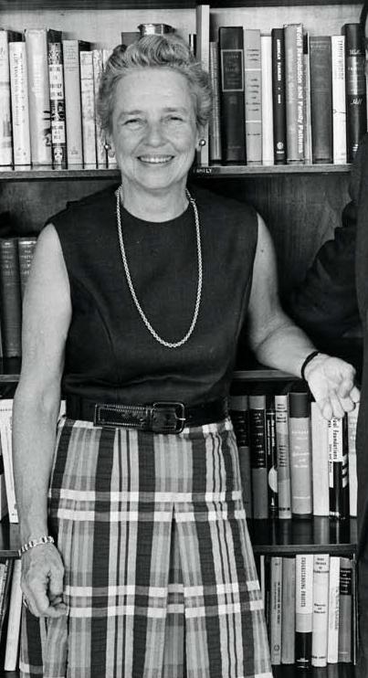 A black & white photo of Riley in front of bookshelf