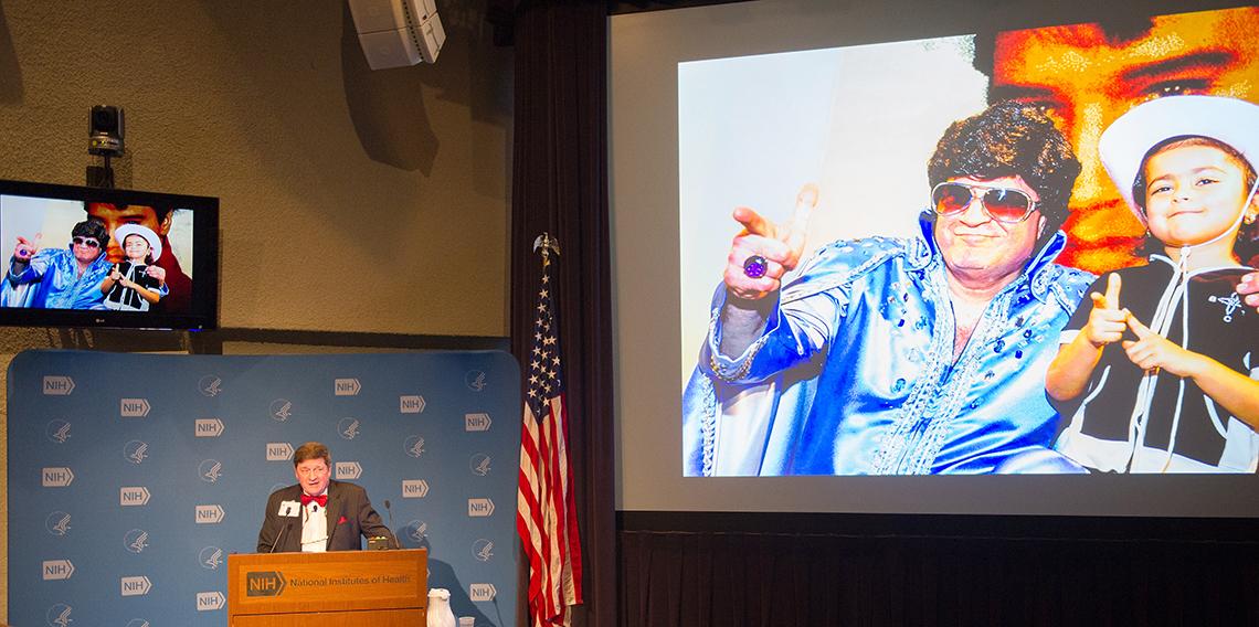 Cohen alongside slide projected of his Elvis impersonation 