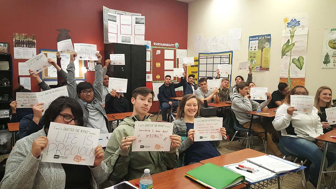Teens hold up “shatter the myths” pledge cards.