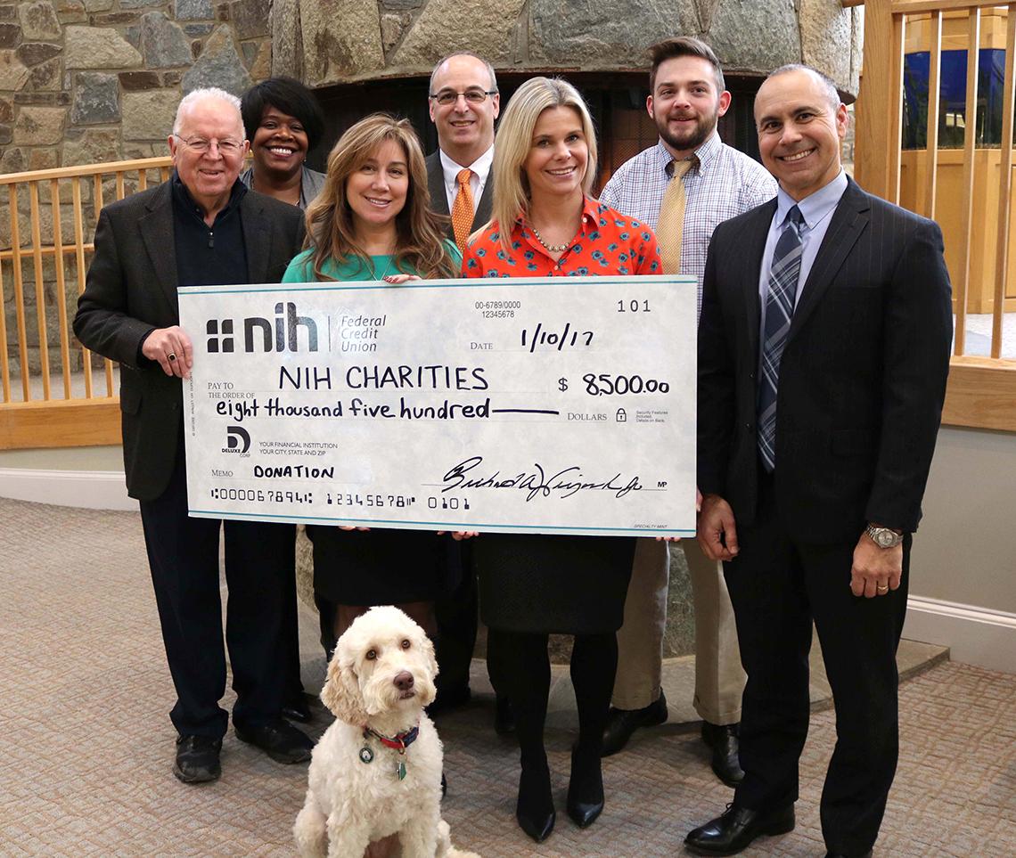 Several people hold up a large check made out to NIH Charities