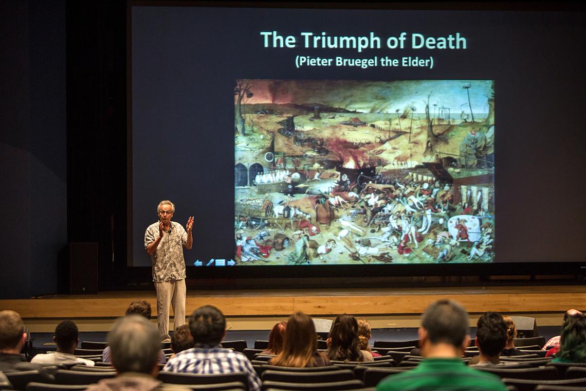 Kolter speaks in front of a slide featuring the painting, The Triumph of Death
