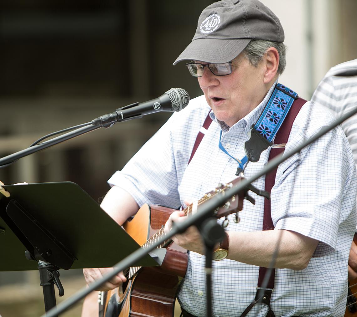 Katz plays guitar and sings into the microphone outside the Clinical Center