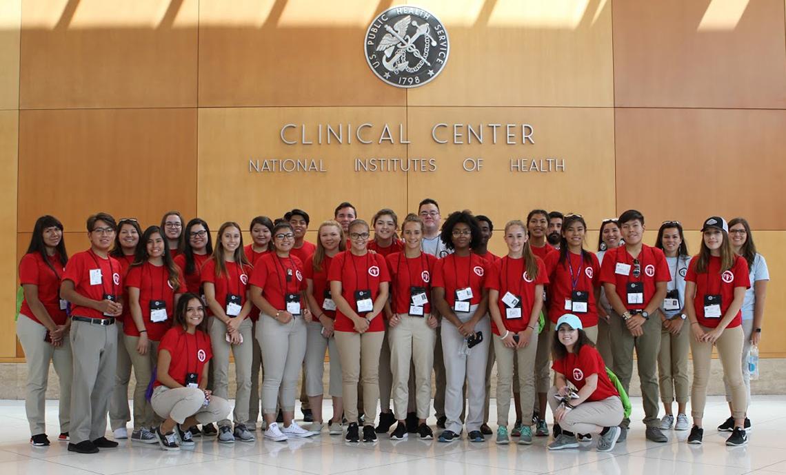 A large group of high school students, dressed in red, pose in the Clinical Center's south lobby.
