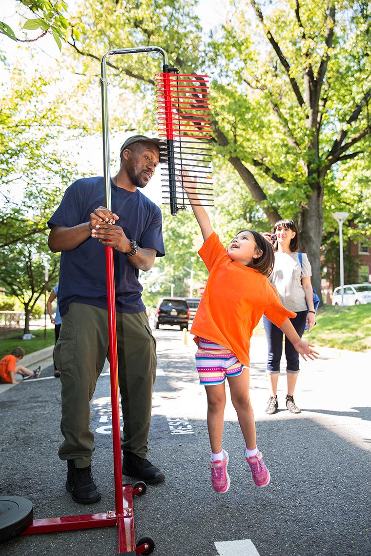 Pesseh helps a child jumping to reach a high marker.