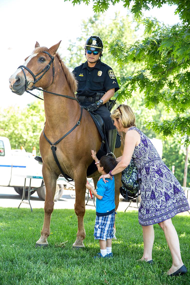 A horse with officer riding is petted by a youngster and adult.