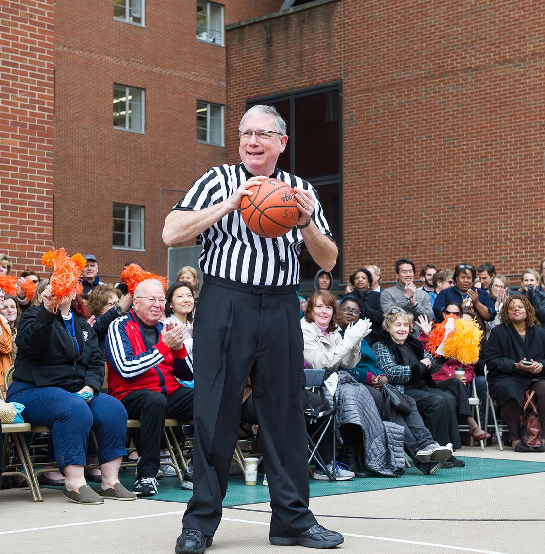 A smiling Tabak stands with basketball in front of crowd.