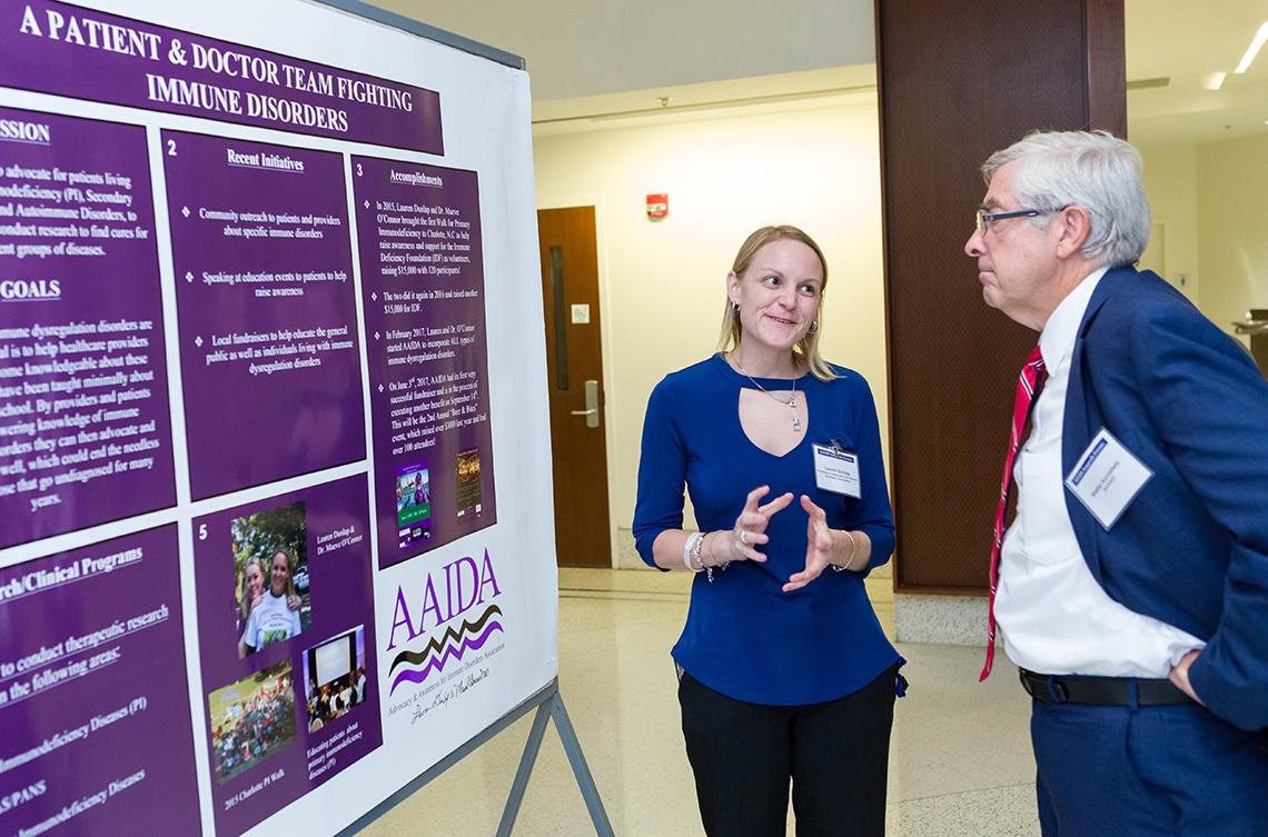 Dunlap stands with Dr. Koroshetz in front of poster with purple panels describing the fight against immune disorders