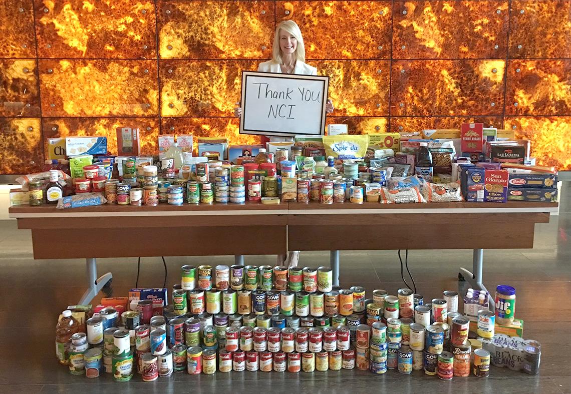 Siegle holds thank you sign behind long table filled with canned goods
