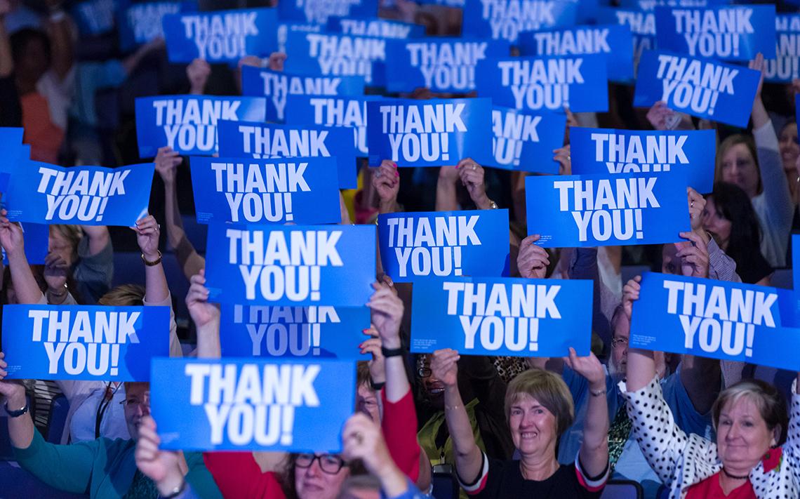 People in crowd hold high blue signs that read, "thank you"