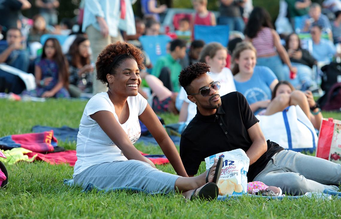 Two NIH'ers relax on the lawn with a bag of potato chips.