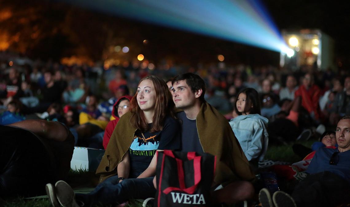 A young couple wrapped in a blanket watches the movie that began after sunset. 