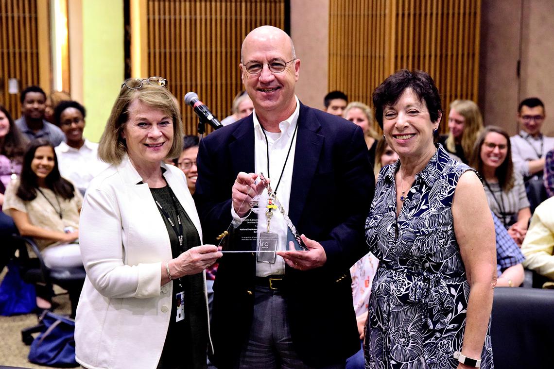Gilman is joined by Birnbaum and Hall. Gilman is holding an award.