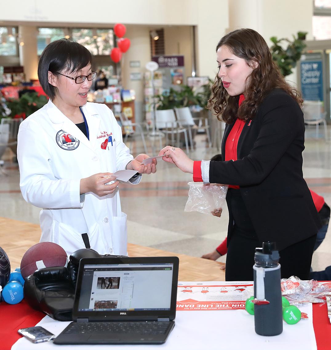Volunteer hands NIH'er a sticker for her heart health pledge