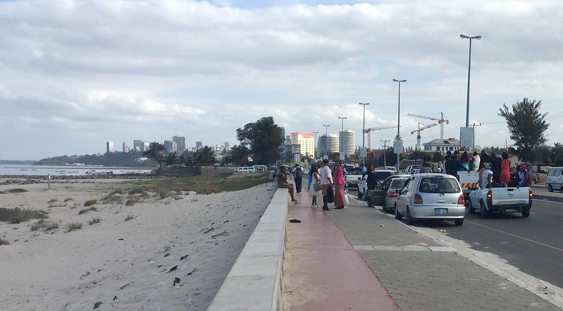 People lined up on sidewalk alongside vehicles in busy traffic