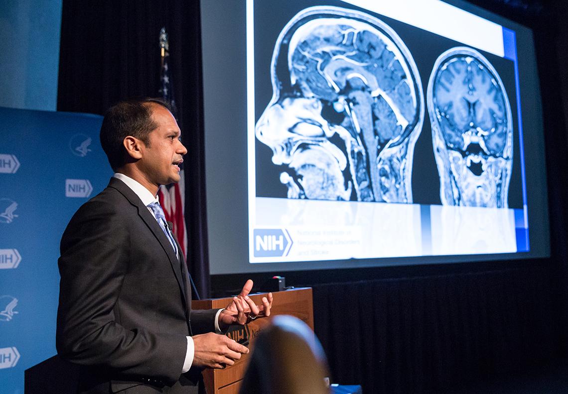 Chittiboina speaking at the podium with brain slide in background