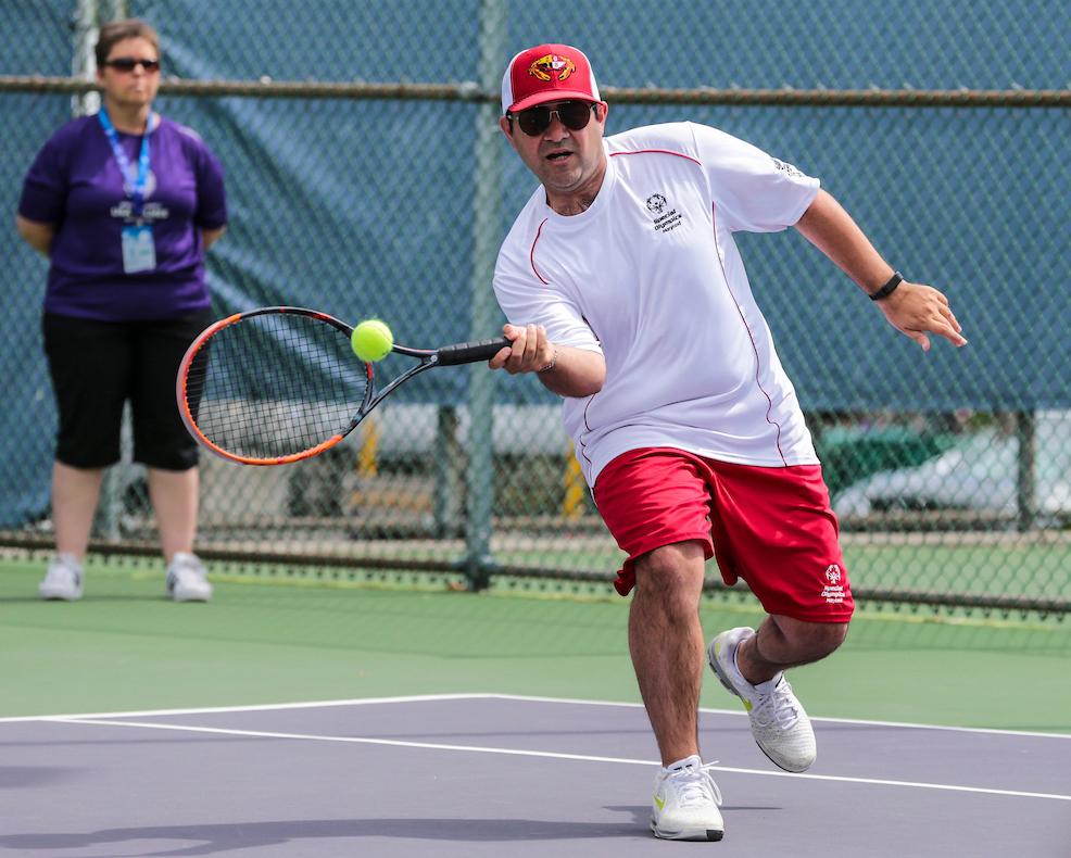 NLM’s Bijan Bagheri hits tennis ball with his racket.