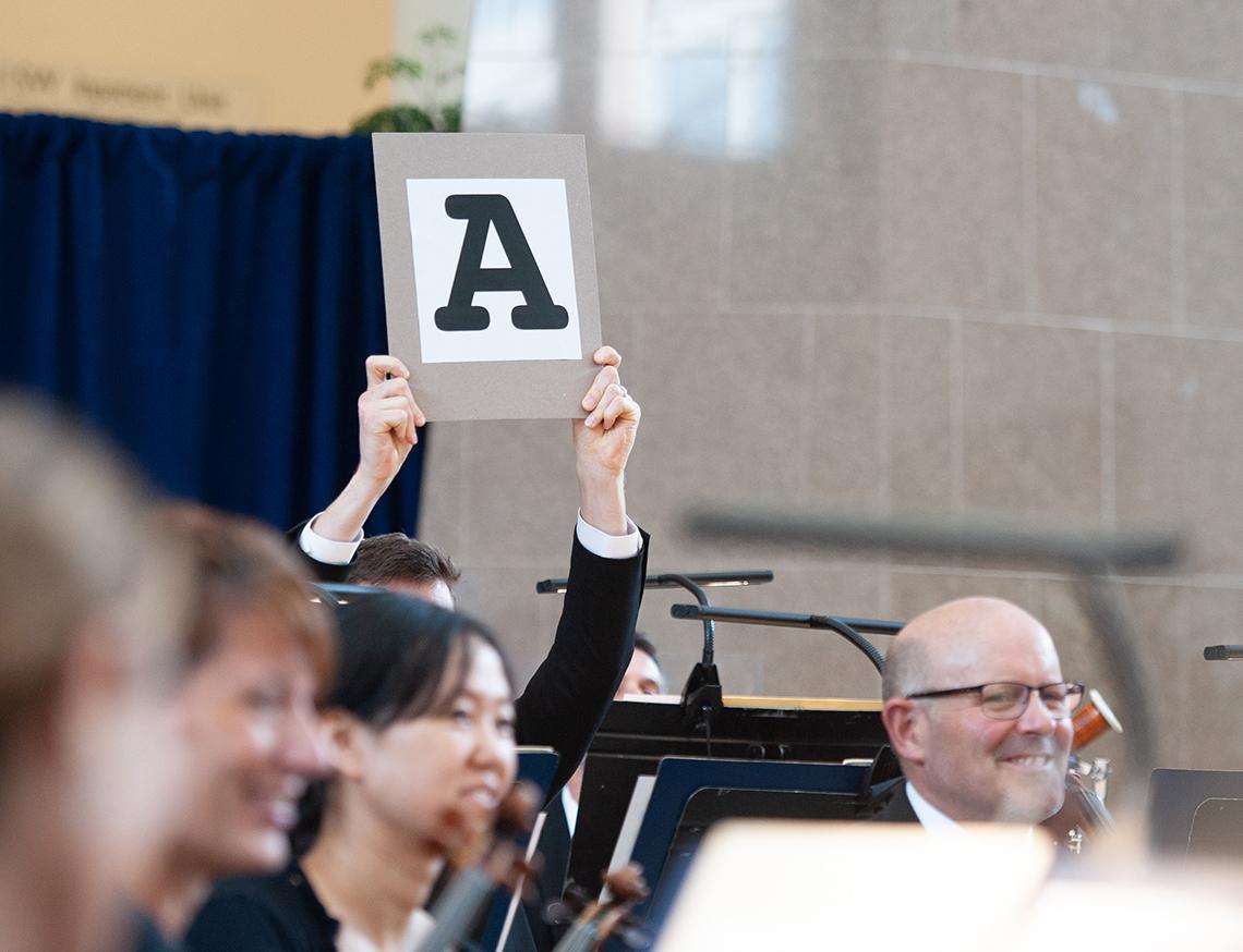 An orchestra member holds up a sign with a large letter "A."