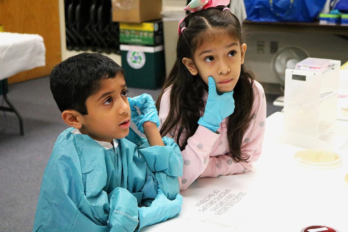 Two siblings of children being treated at NIH listen attentively while seated at at table.