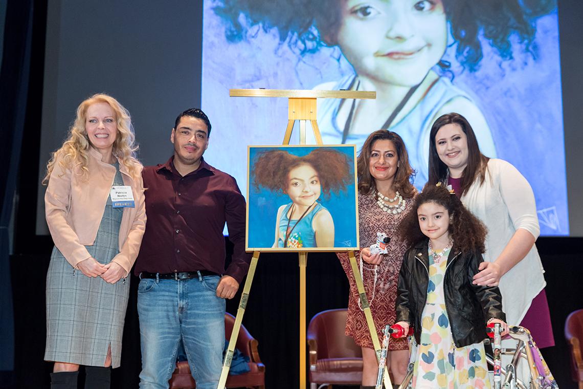 Weltin, surrounded by Amber's family and Feinberg, presents a painting featuring Amber to the rare patient art collection