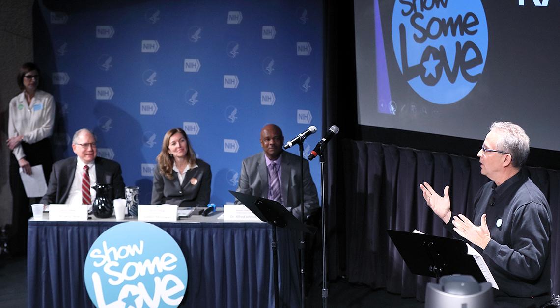 Three people sit behind a table watching the show's emcee
