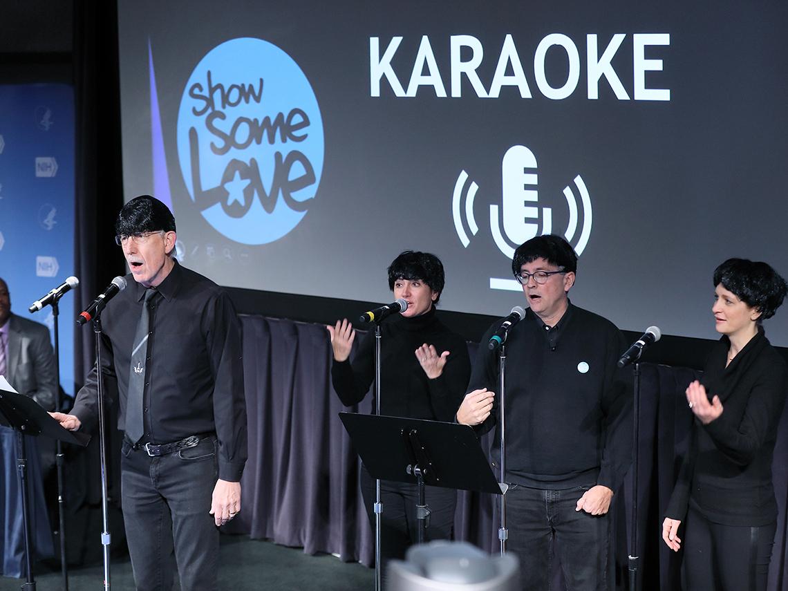 Four people wearing black Beatles'style wigs sing on stage