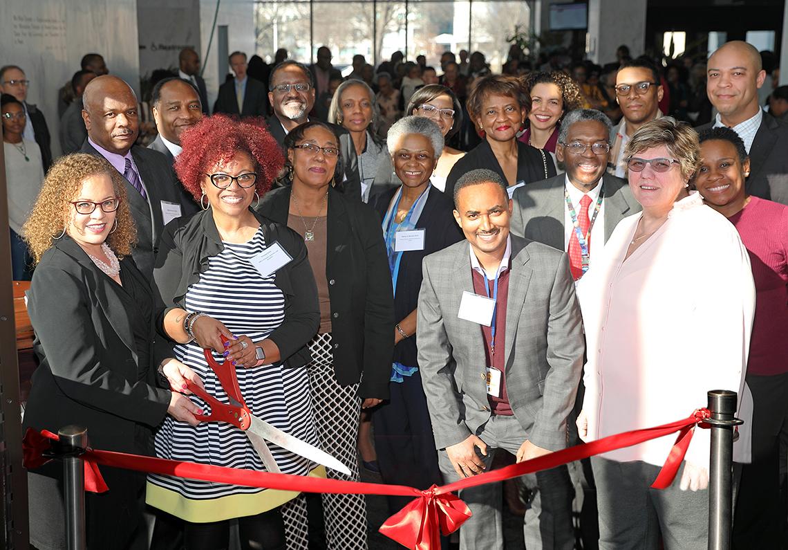 A smiling group of NIH'ers hold big scissors to cut the red ribbon marking the exhibit's opening.