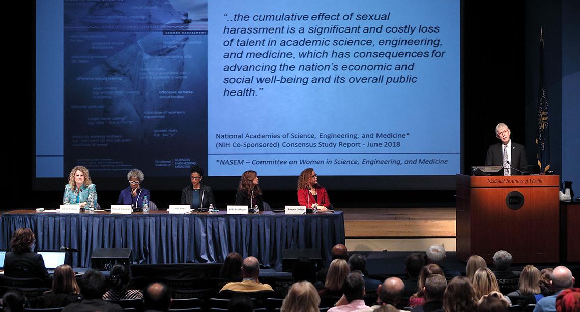 Dr. Collins speaks from podium with panelists seated nearby in front of slide that warns of the cumulative, costly effects of sexual harassment.