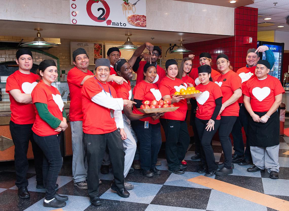 The smiling cafeteria staff from Bldg. 10 hold out trays of fruit