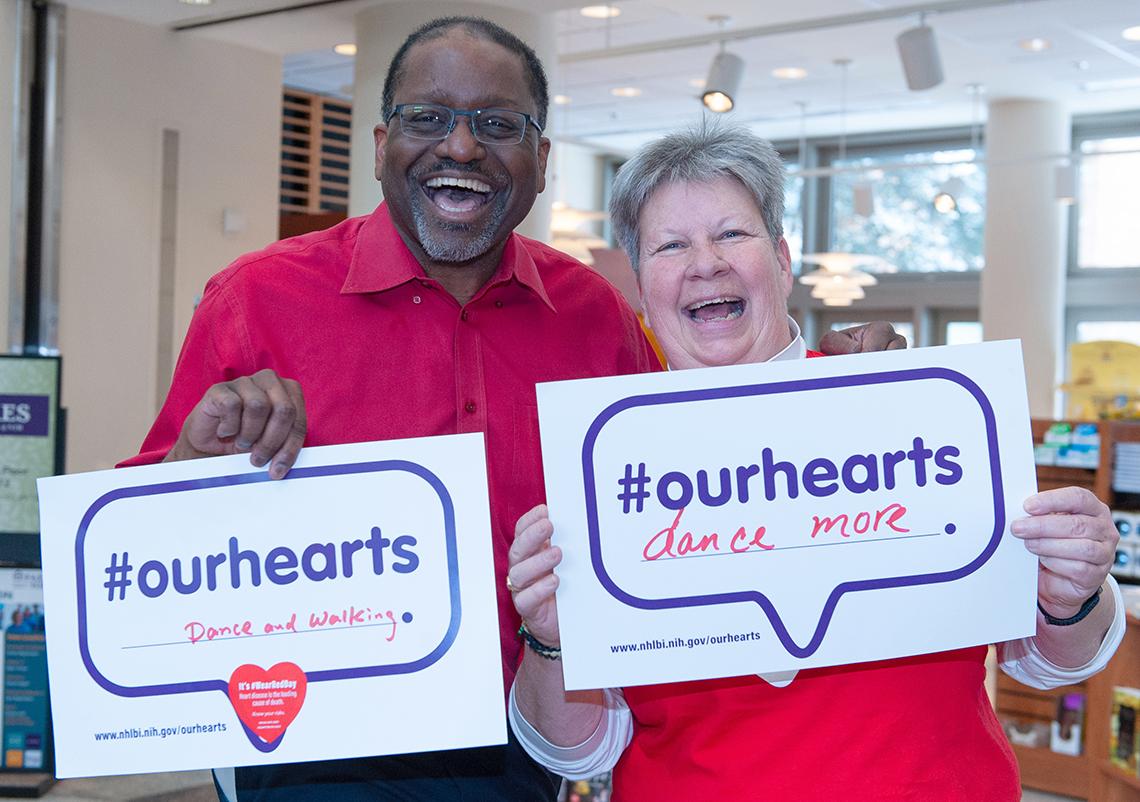 NHLBI director Dr. Gibbons poses with colleague, holding sign pledging to dance and walk more.