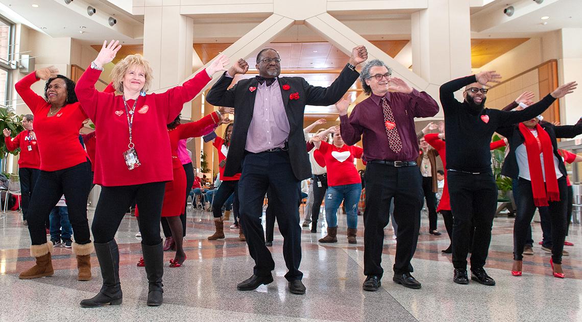 NHLBI and NIMHD directors and colleagues wave arms high in dance in Clinical Center's atrium.