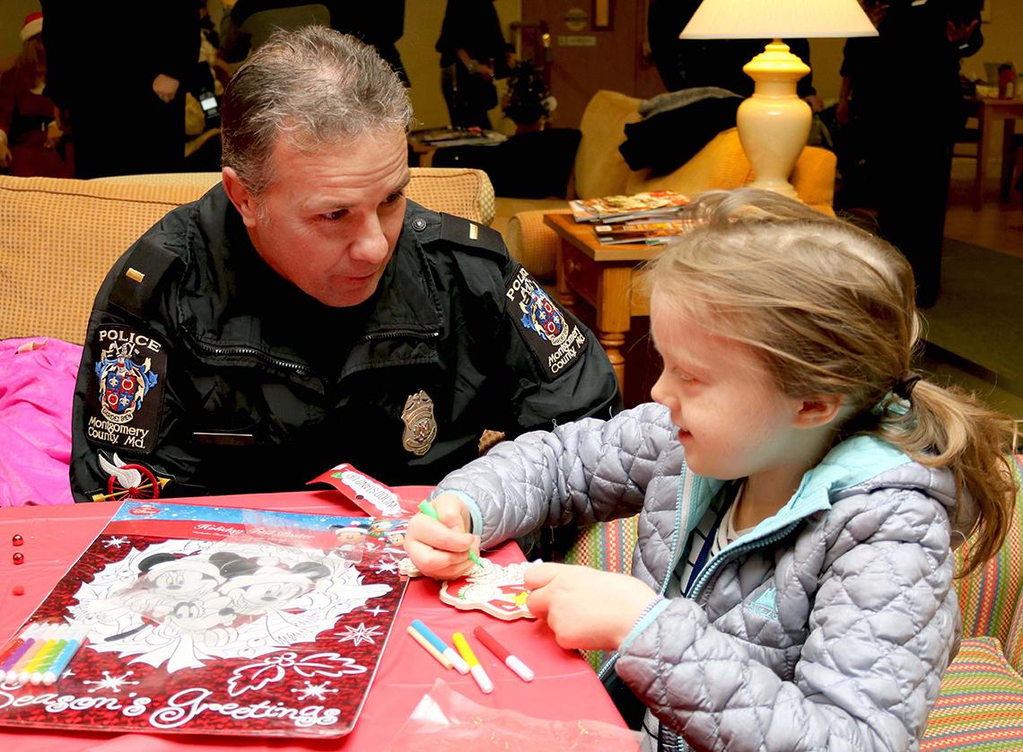 Policeman at table, talking with a young child at a holiday party.