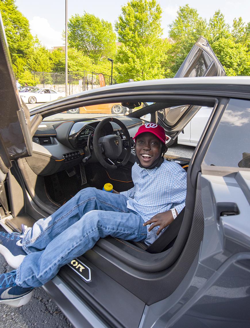 Smiling youngster sits in the driver's seat of a luxury sportscar.