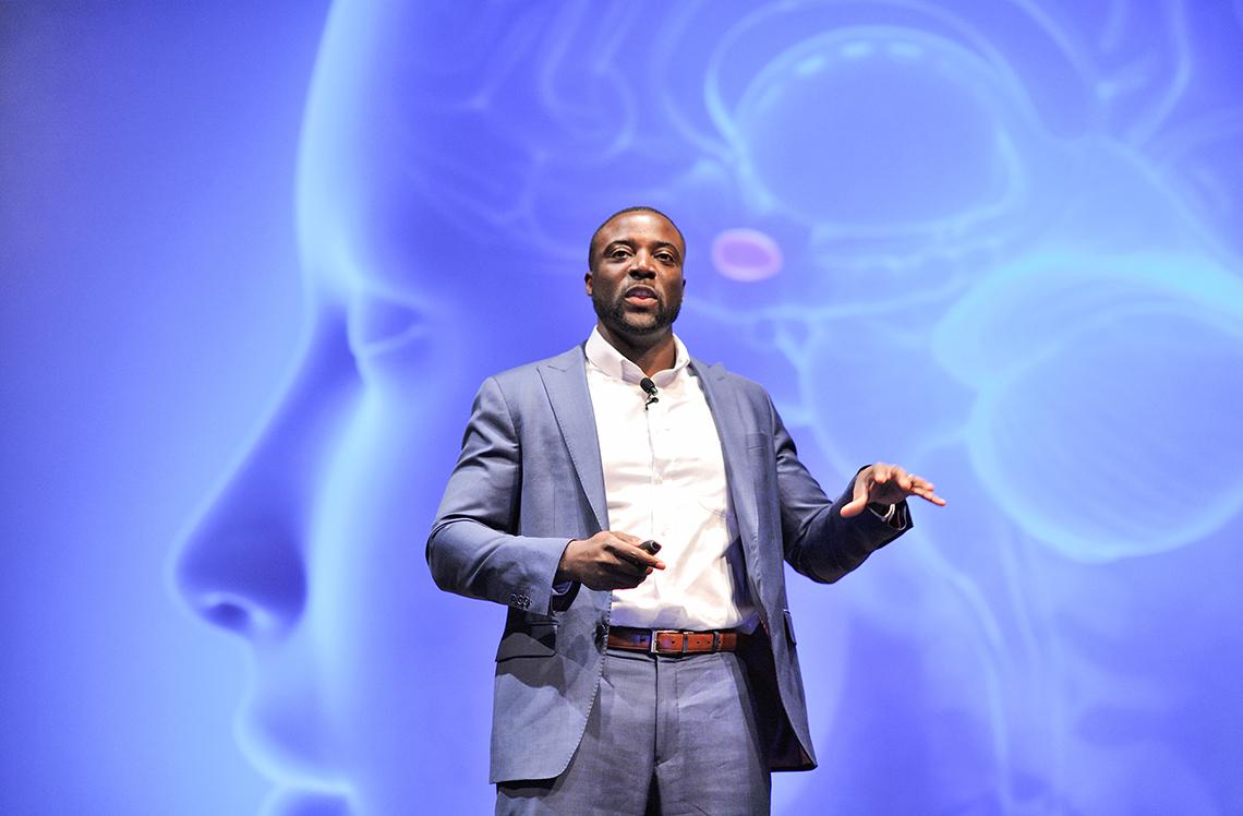 Christian stands in front of projected slide of human brain illustration 