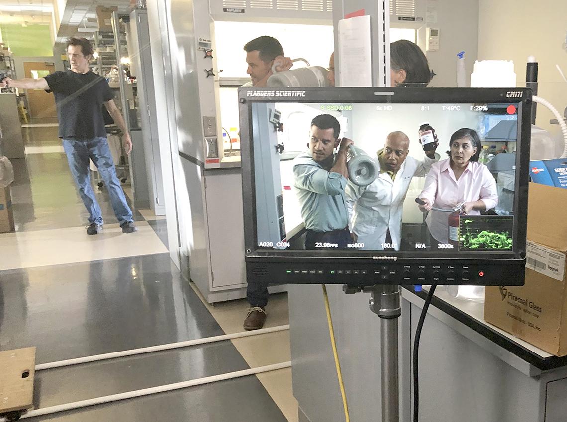 Camera monitor showing actors posing with makeshift weapons found in a lab environment