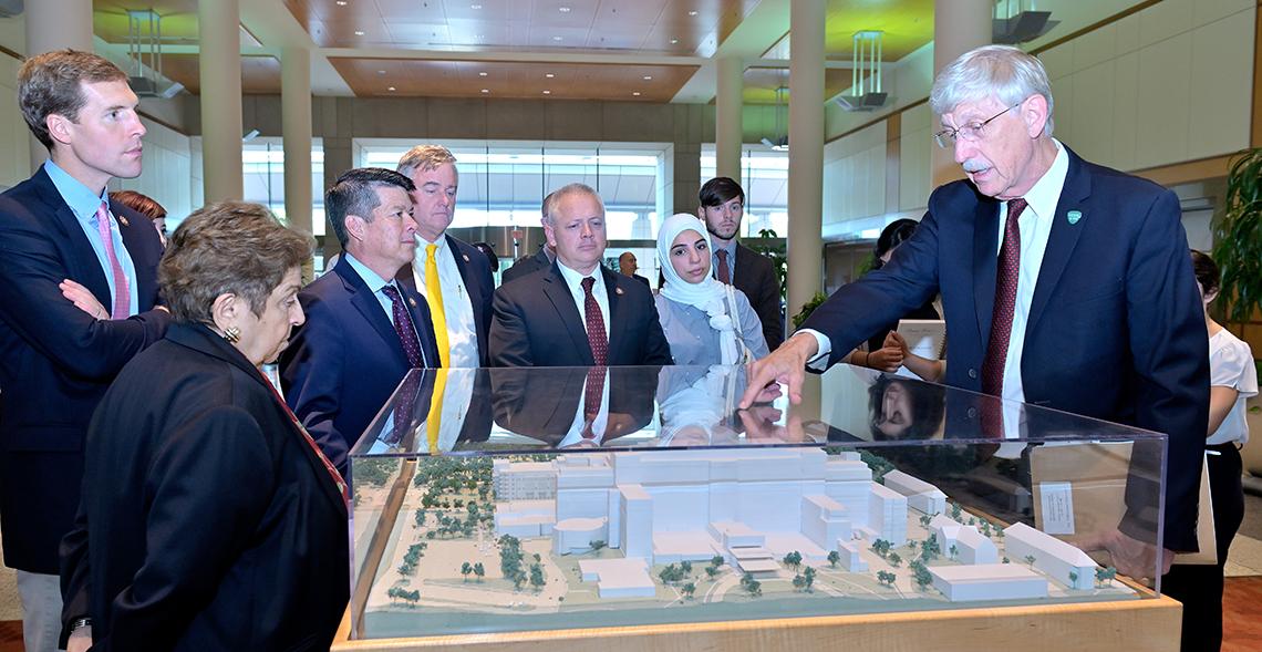 Collins points to the Clinical Center model in the CRC atrium while talking with Members of Congress.