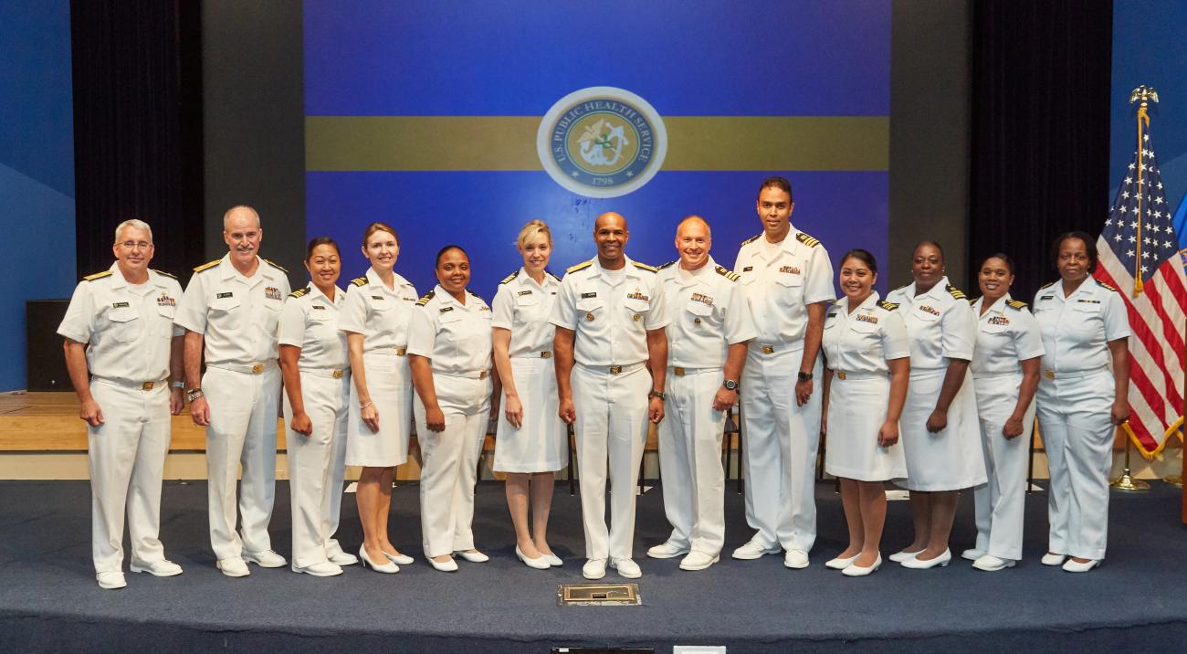 Dressed in their white uniforms, recently promoted NIH Commissioned Corps officers pose with the surgeon general.