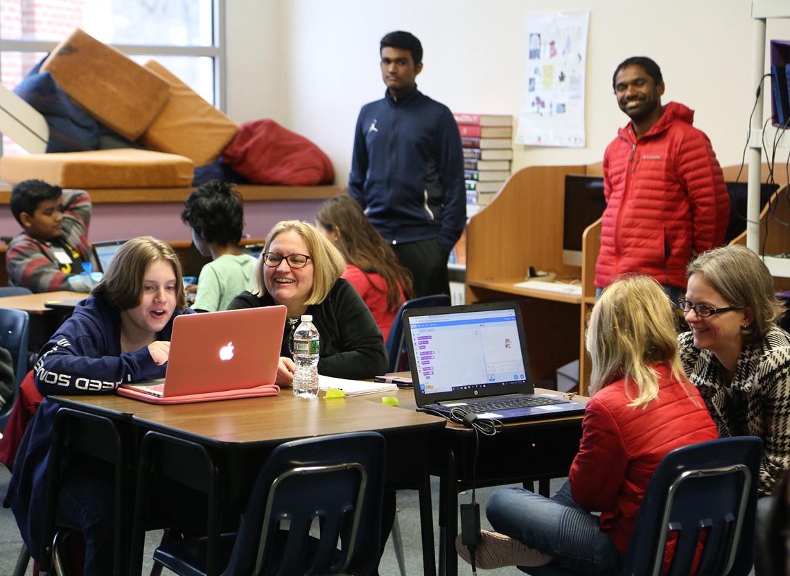 Students play computer coding game on laptops, guided by NIH postdocs and other staff.